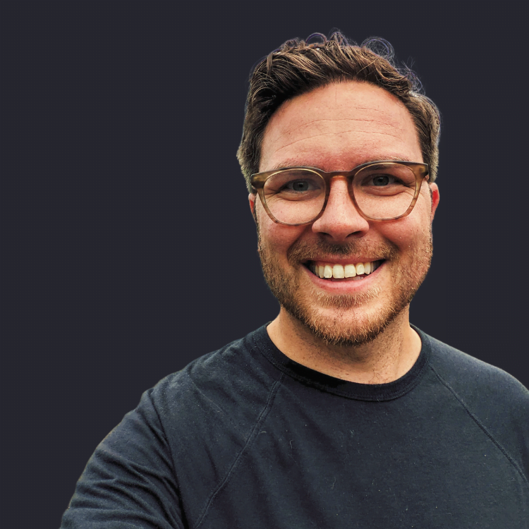 A picture of Charles Howes smiling wearing a black shirt and glasses.
